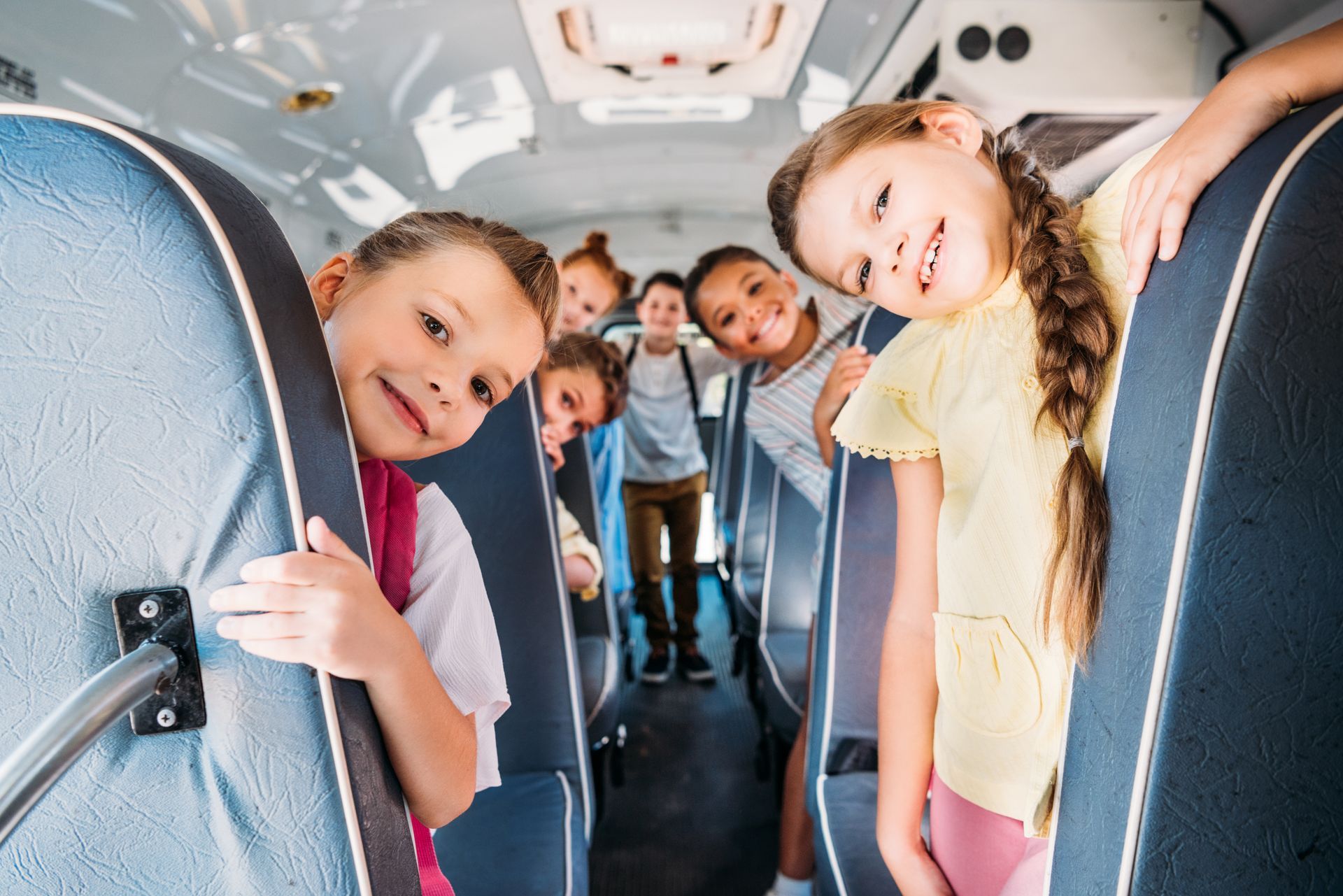 group of cute schoolchildren riding on school bus and looking at camera.
