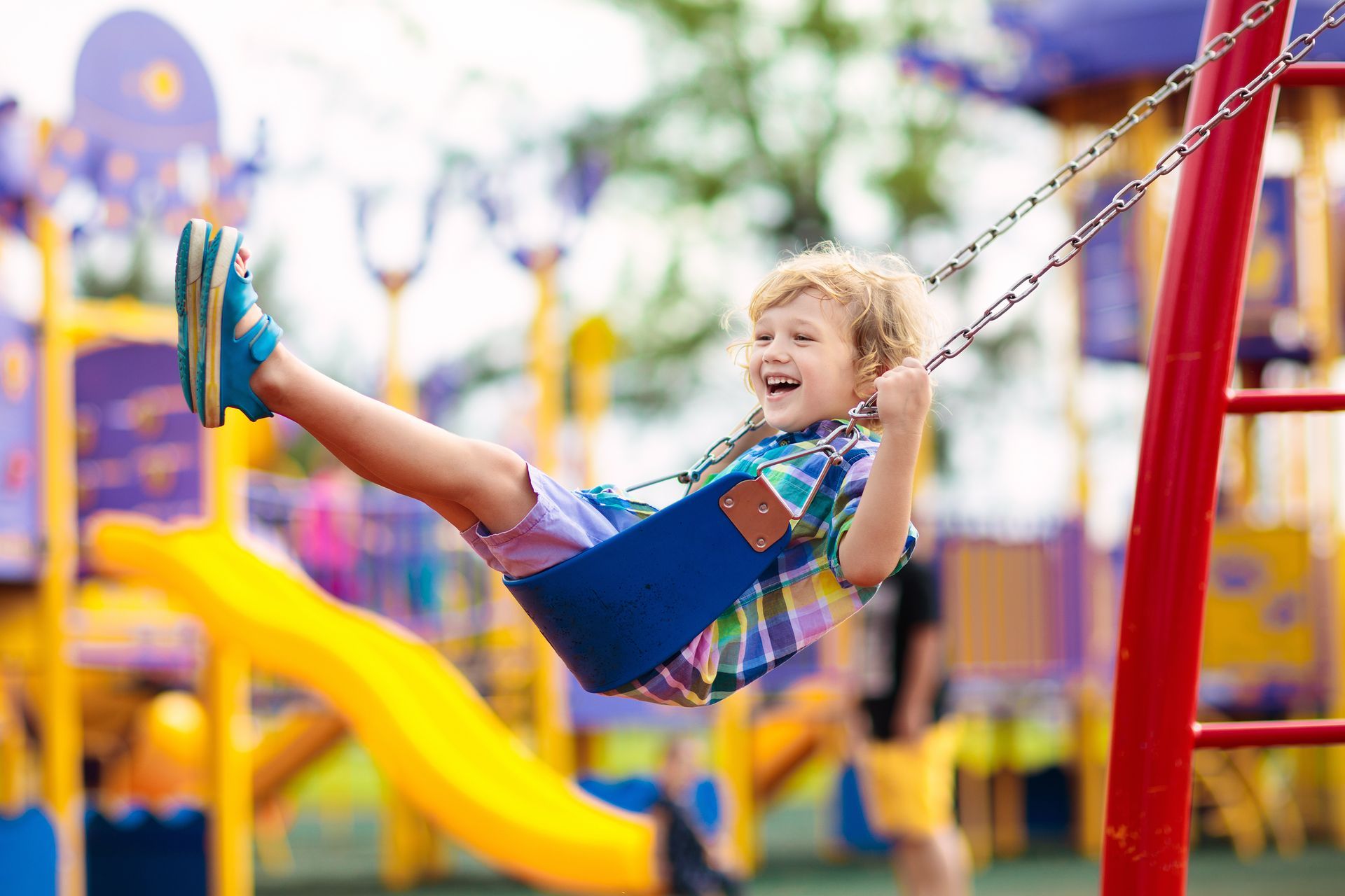 Child on swing playing on outdoor playground. Kids play on school or kindergarten yard. Active kid swinging. Healthy summer activity for children. Little boy having fun outdoors.