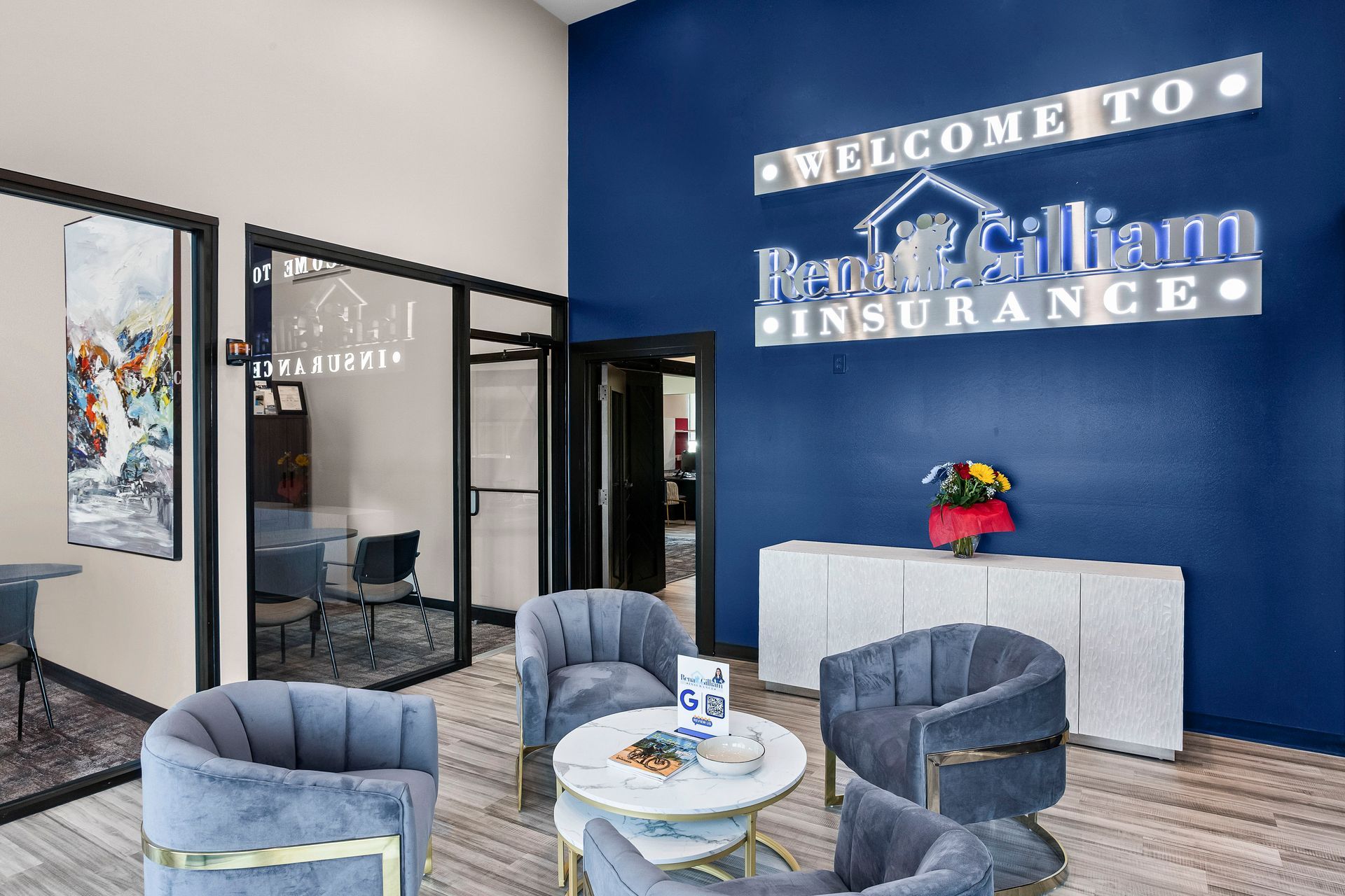 Reception area for Rena Gilliam Insurance with blue wall and logo, gray chairs, and white table.
