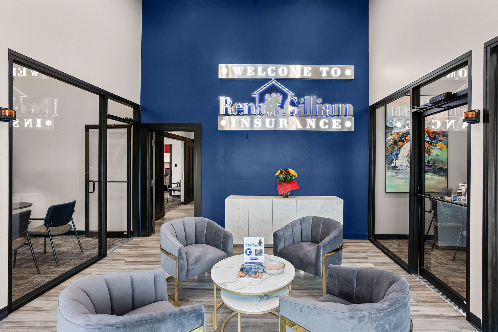 Blue and white insurance office lobby with seating, welcome sign, and glass-walled rooms.