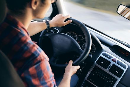 Person driving a car, hands on steering wheel. Inside car with dashboard visible.