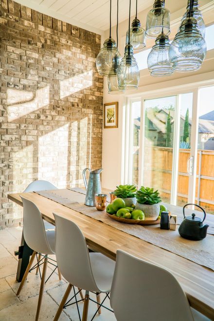 Dining room with wood table, white chairs, brick wall, glass pendant lights, and sliding glass door.