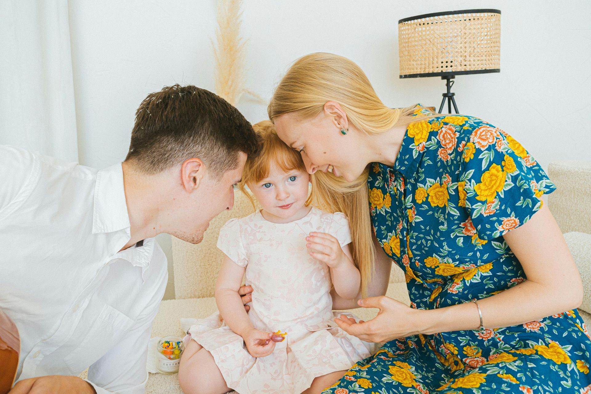 Family of three smiling, embracing on a couch. A child sits between parents, who look down adoringly.