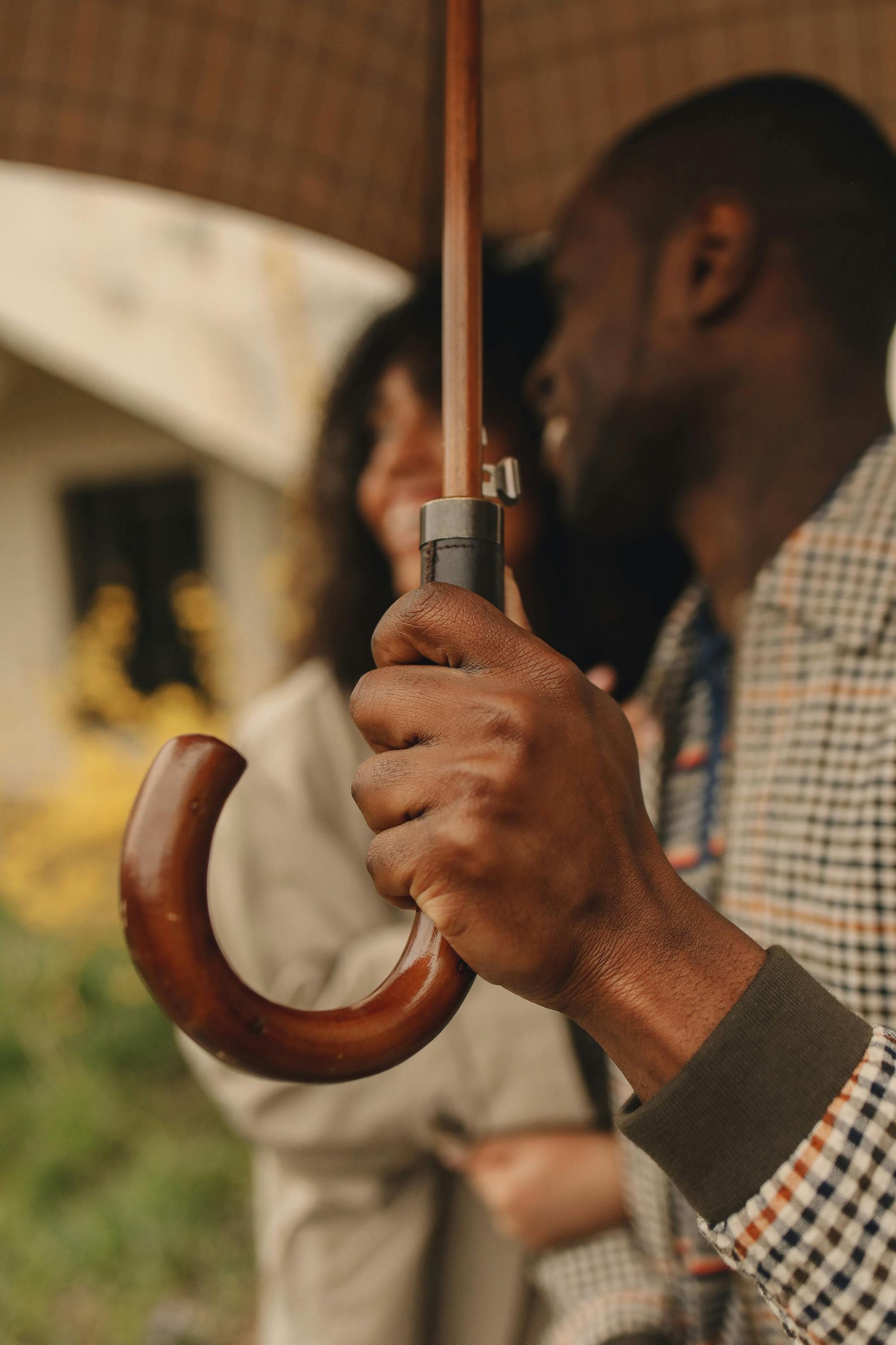 Man holding a brown umbrella handle, smiling, with a blurred person behind him.