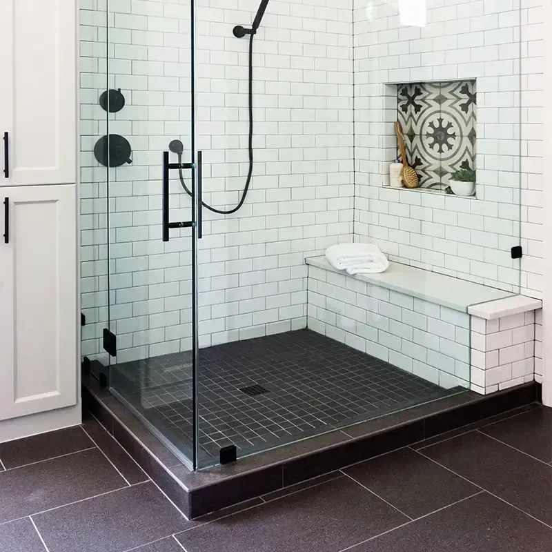 Modern bathroom with glass shower enclosure, black fixtures, and built-in bench.