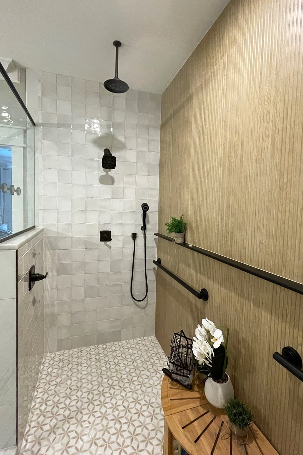 Modern shower with white tiled walls, wooden accent wall, black fixtures, and a wooden bench.