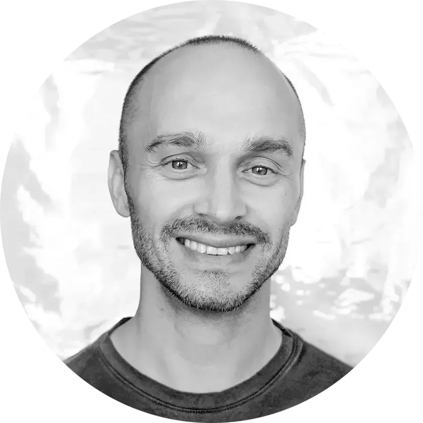 Bald man with a trimmed beard smiles, looking directly at the camera.