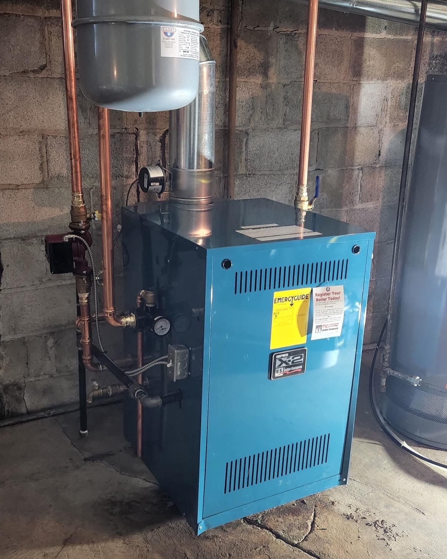 A blue boiler is sitting in a basement next to a water heater.
