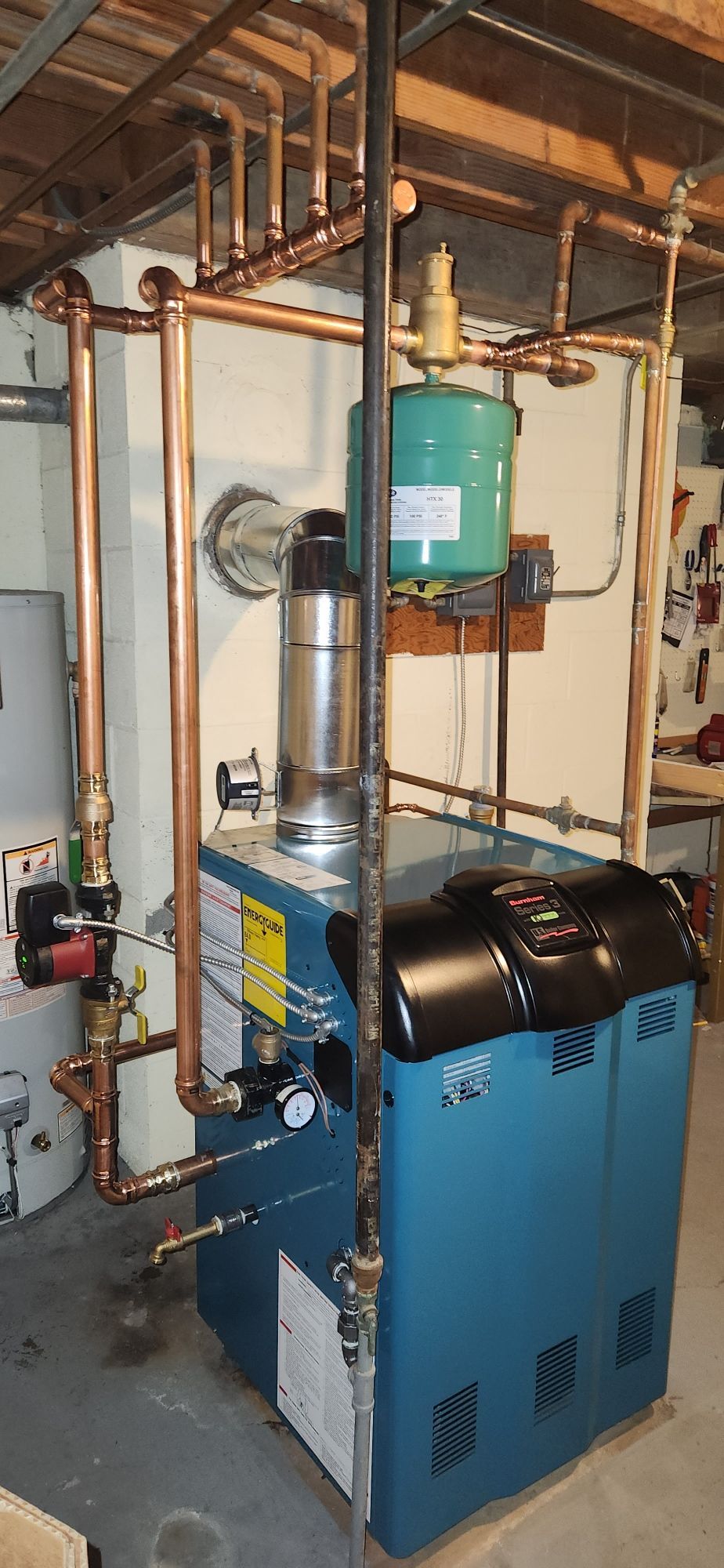 A blue boiler is sitting in a basement next to a water heater.
