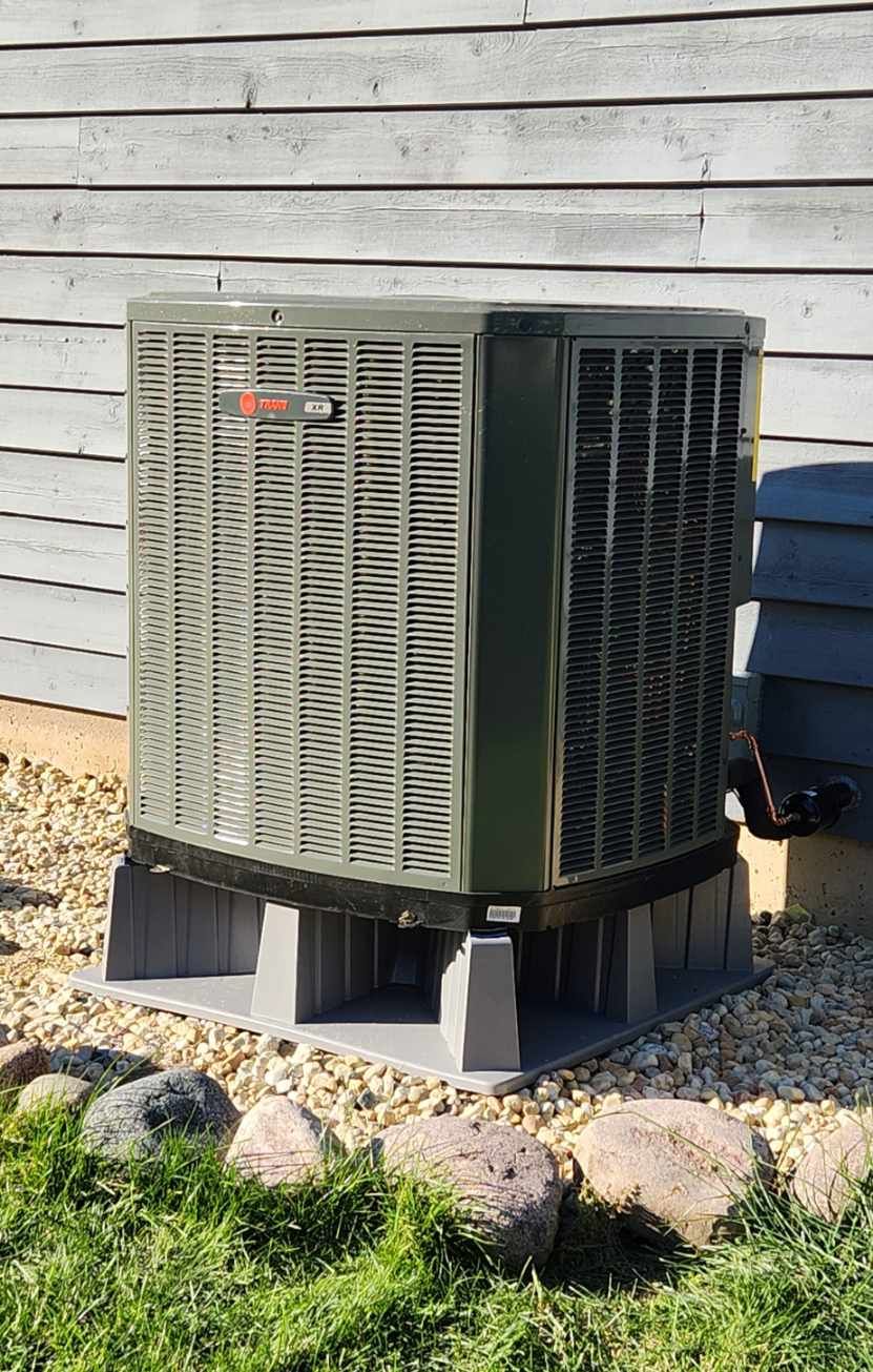 A large air conditioner is sitting on top of a concrete block in front of a house.