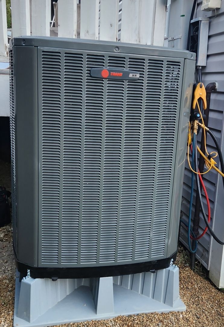 A large gray air conditioner is sitting outside of a house.