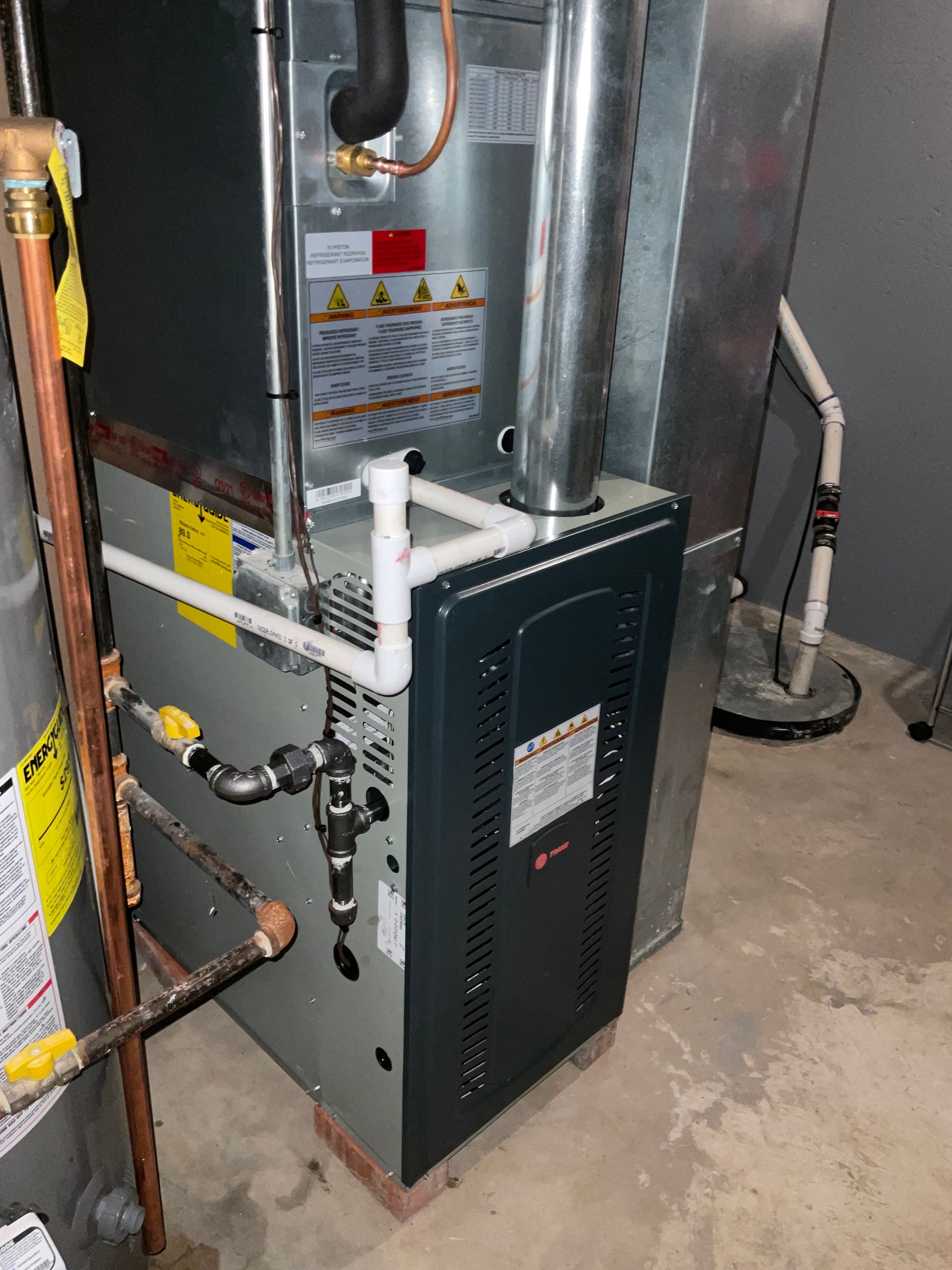 An air conditioner is sitting in a basement next to a water heater.