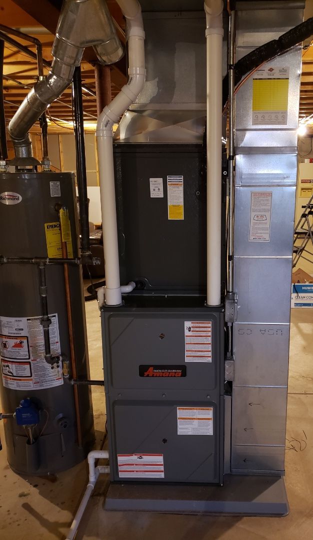 A furnace is sitting in a basement next to a water heater.