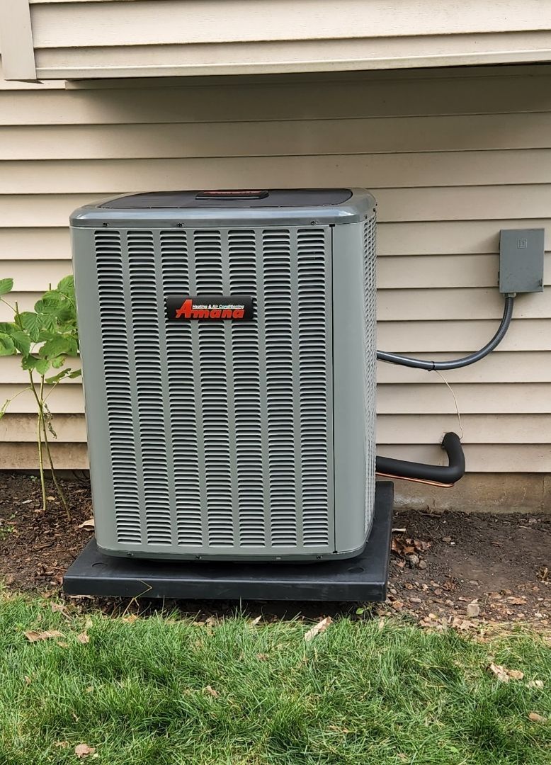 A large air conditioner is sitting on top of a concrete platform next to a house.
