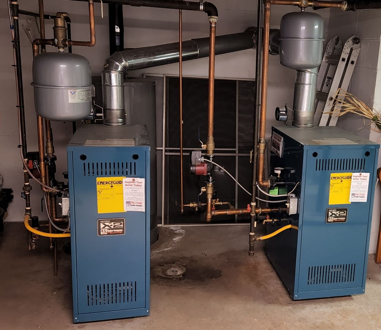 Two blue boilers in a room with copper pipes