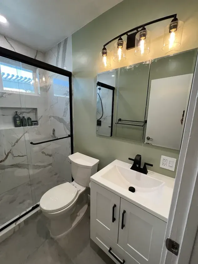 A bathroom with a toilet, sink, mirror and shower.