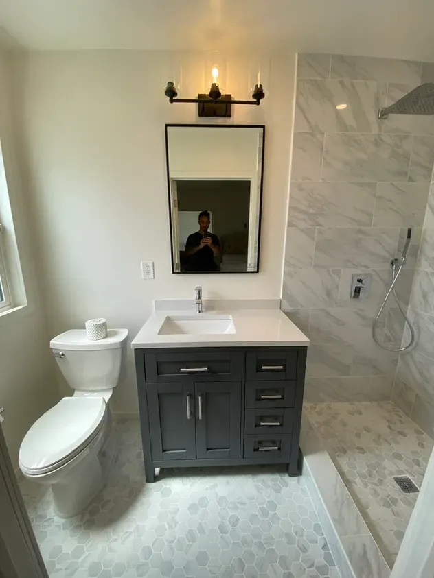 A bathroom with a toilet, sink, mirror and shower.