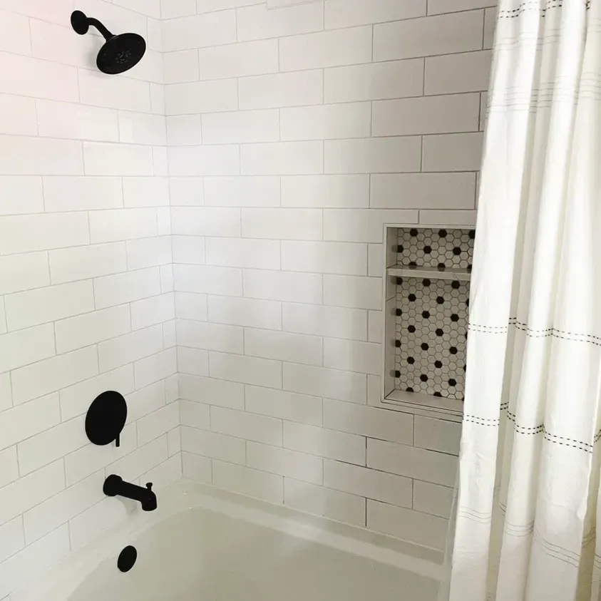 A bathroom with white tiles, black shower heads and a white shower curtain.