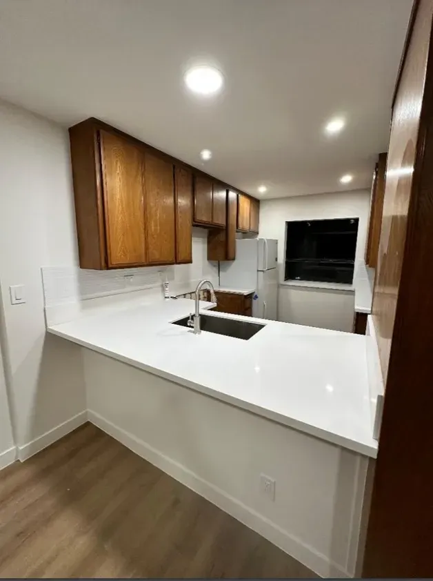 A kitchen with wooden cabinets , white counter tops , a sink and a refrigerator.