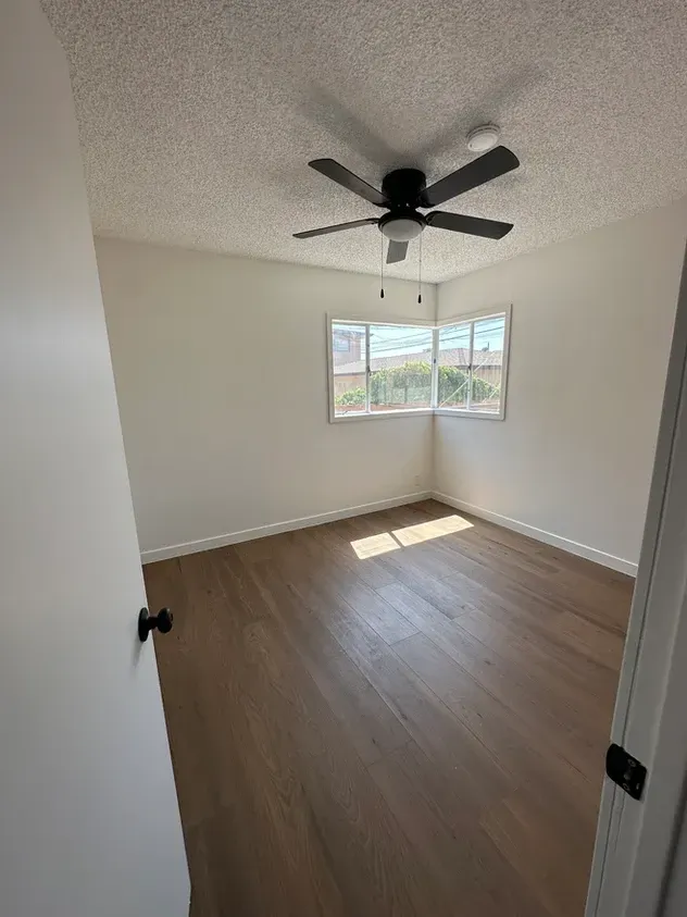An empty bedroom with hardwood floors and a ceiling fan.