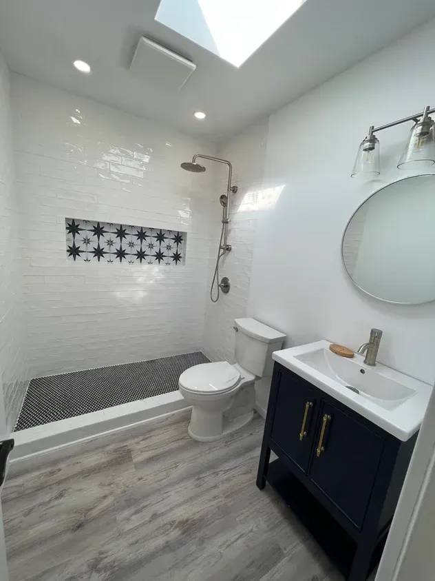 A bathroom with a toilet, sink, shower and skylight.