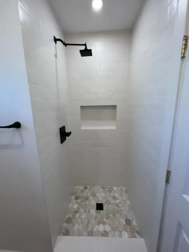 A bathroom with a walk in shower with a black shower head.