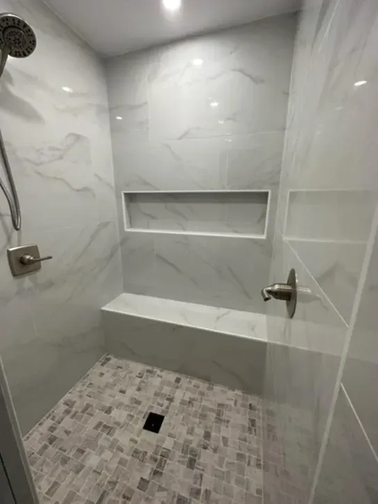 A shower with a bench and a shower head in a bathroom.
