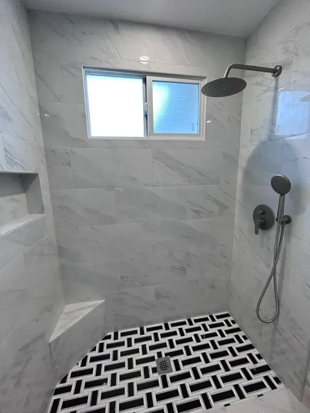 A shower with a black and white tile floor and a window.