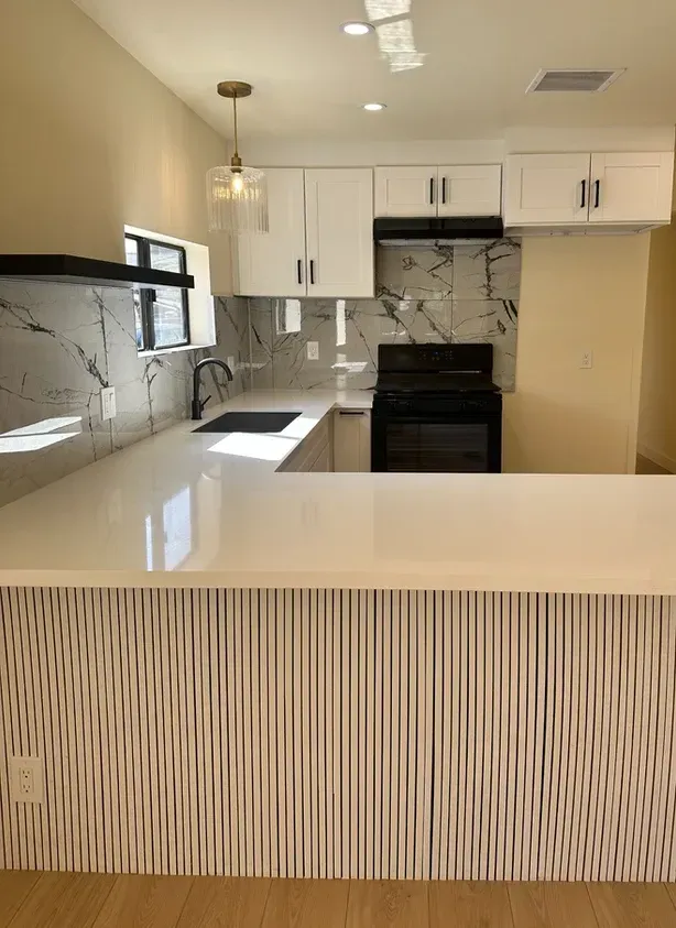 A kitchen with white cabinets, a stove, a sink, and a counter.