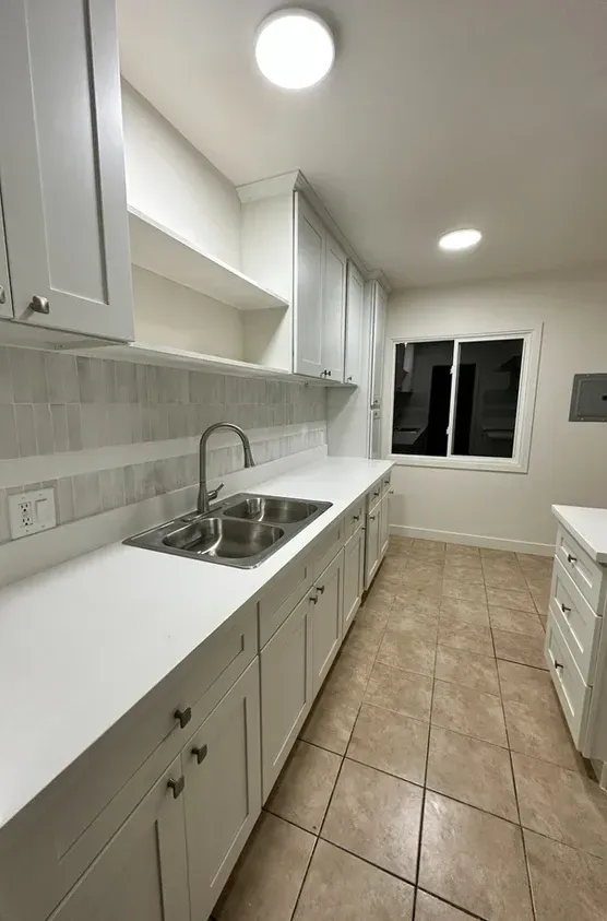 A kitchen with white cabinets, a sink, and a window.