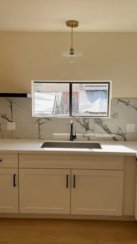 A kitchen with white cabinets, a sink, and a window.