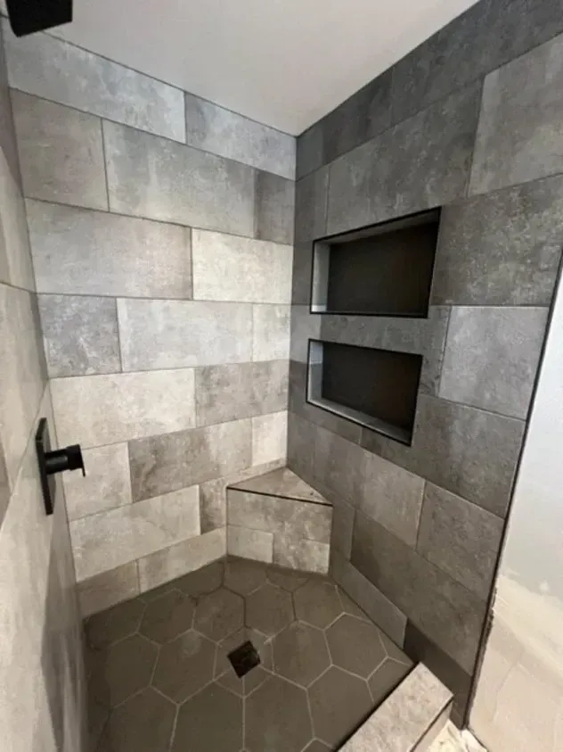 A shower with a corner shelf and gray tiles on the wall.