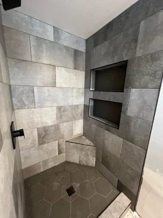 A shower with a corner shelf and a black shower head.