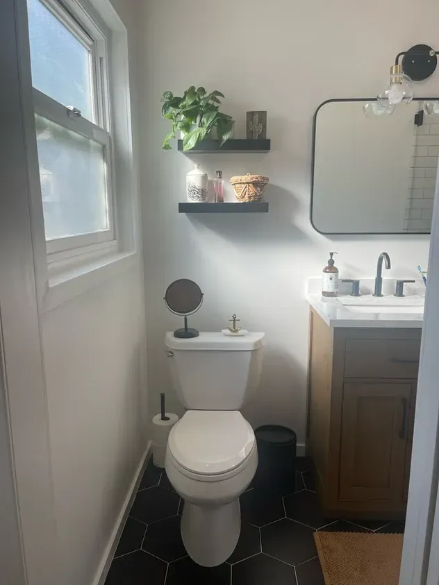 A bathroom with a toilet, sink, mirror and window.