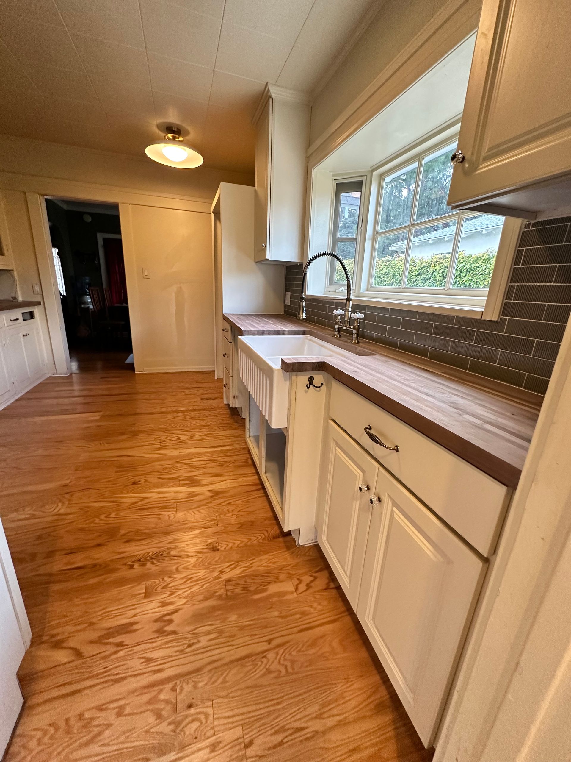 A kitchen with hardwood floors , white cabinets , a sink and a window.