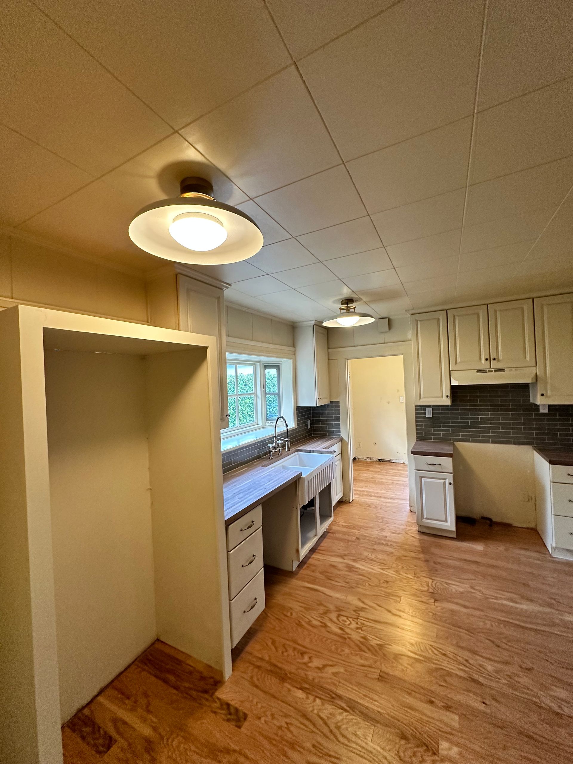 An empty kitchen with hardwood floors and white cabinets