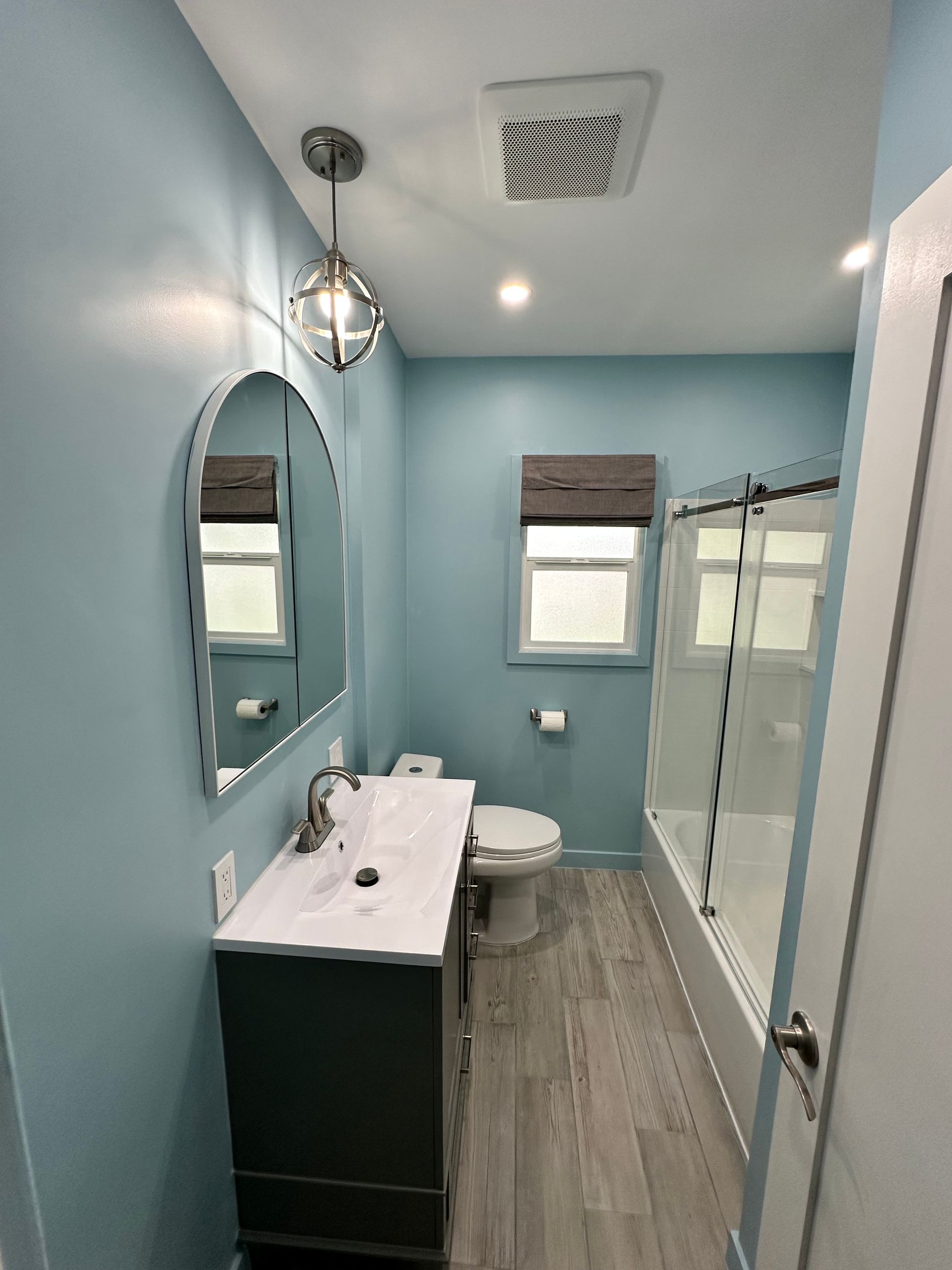 A bathroom with blue walls , a sink , toilet , and shower.