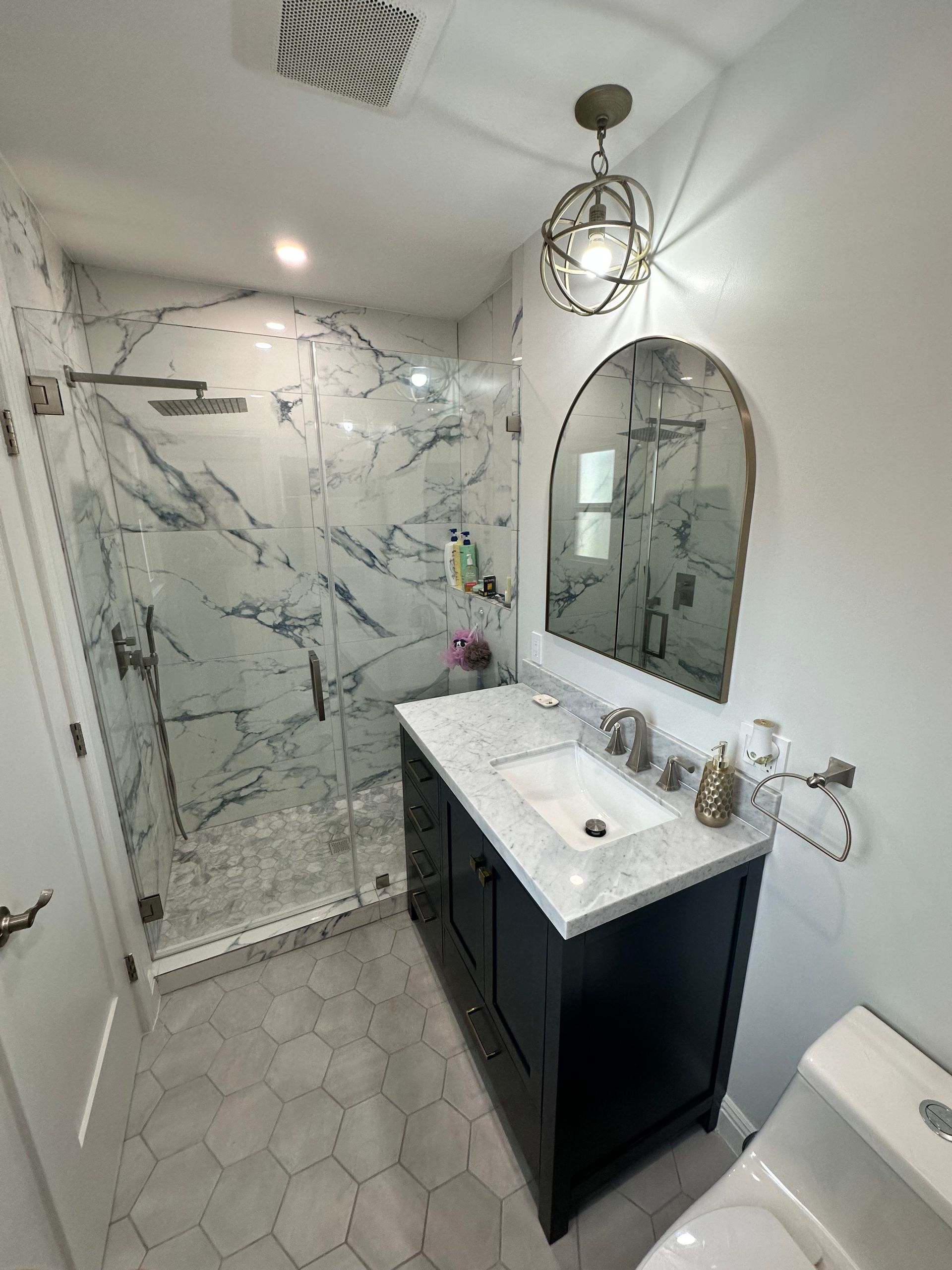 A bathroom with a sink , toilet , shower and mirror.