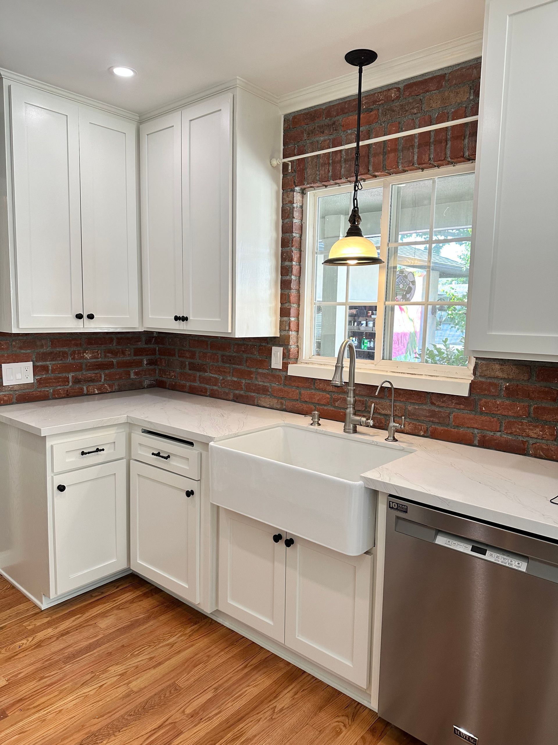A kitchen with white cabinets, a farmhouse sink, a stainless steel dishwasher and a window.