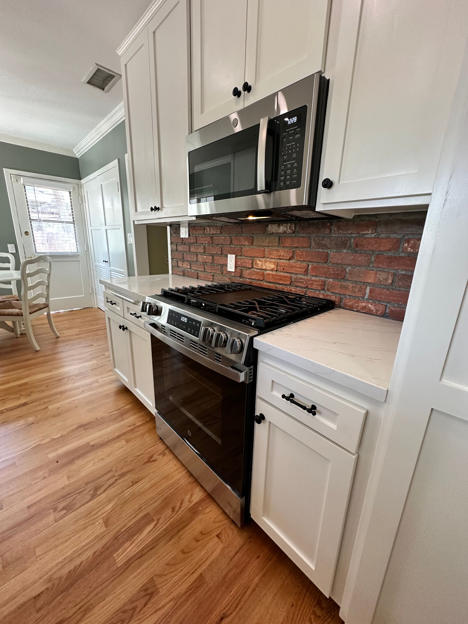 A kitchen with white cabinets, a stove, a microwave, and a brick wall.