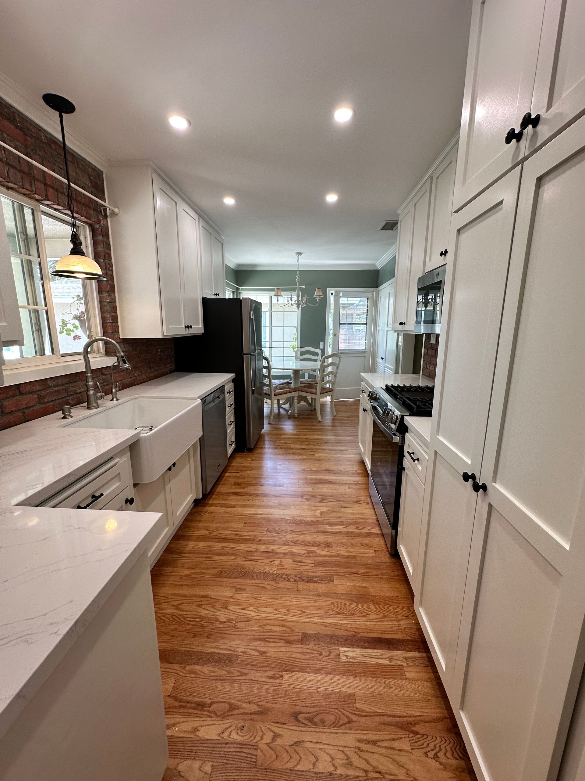 A kitchen with white cabinets and hardwood floors leading to a dining room.