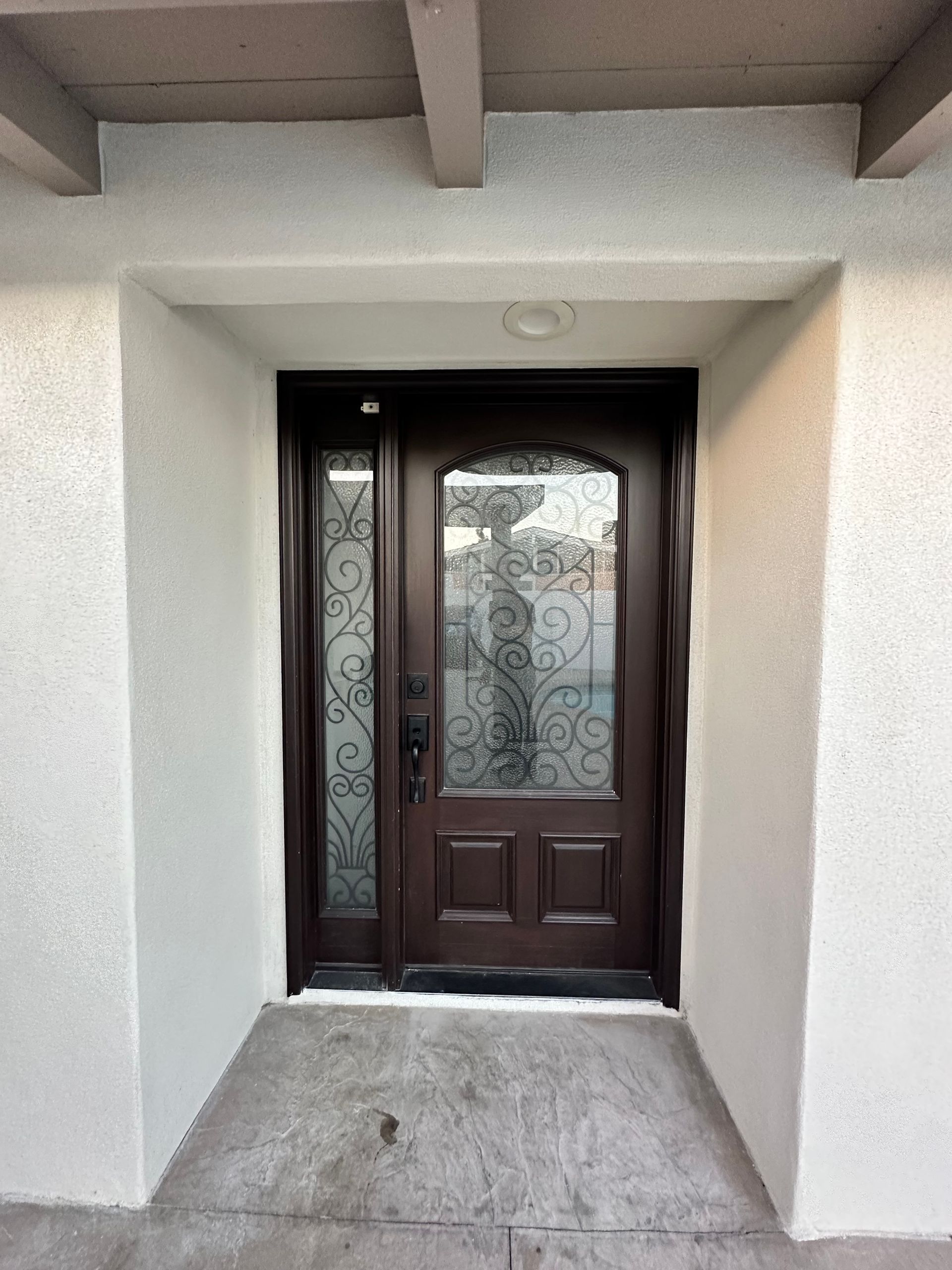 A brown door with a wrought iron frame is on a white wall.