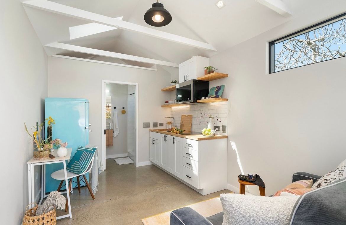 A living room with a couch , chair , desk and kitchen.