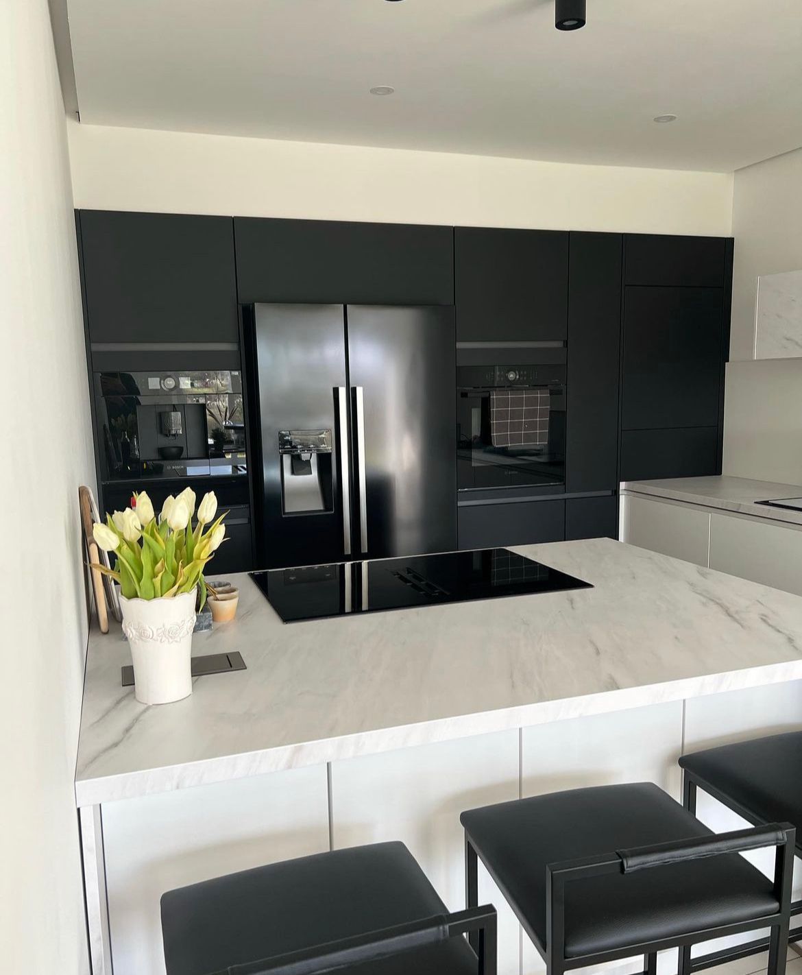 A kitchen with black cabinets , a black refrigerator , a stove top oven , and a marble counter top.