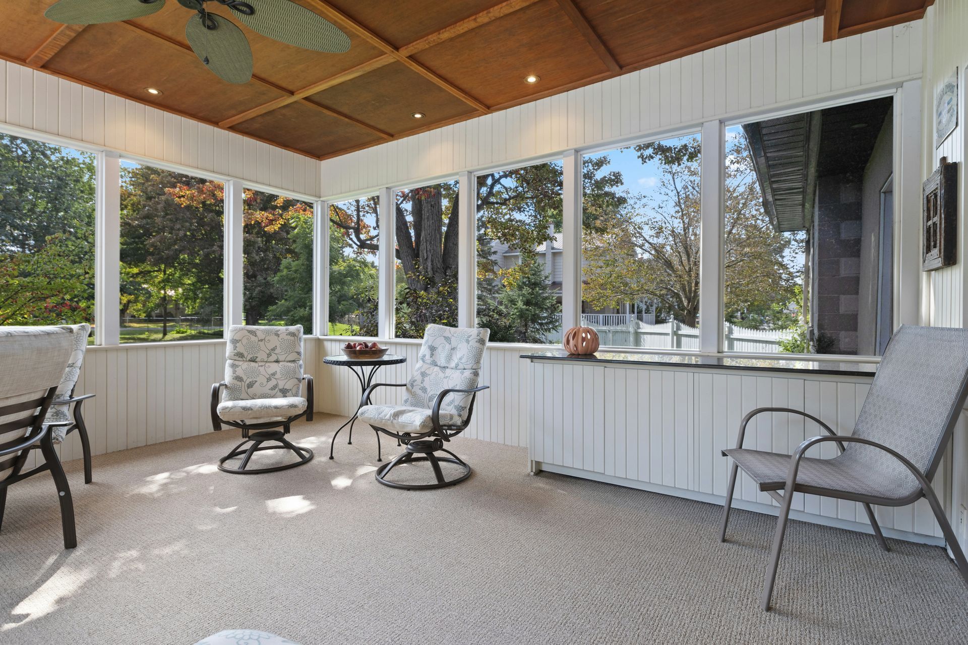 A screened in porch with chairs , a table and a ceiling fan.
