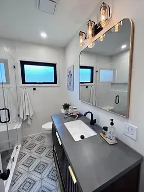 A bathroom with a sink, toilet, shower and mirror.