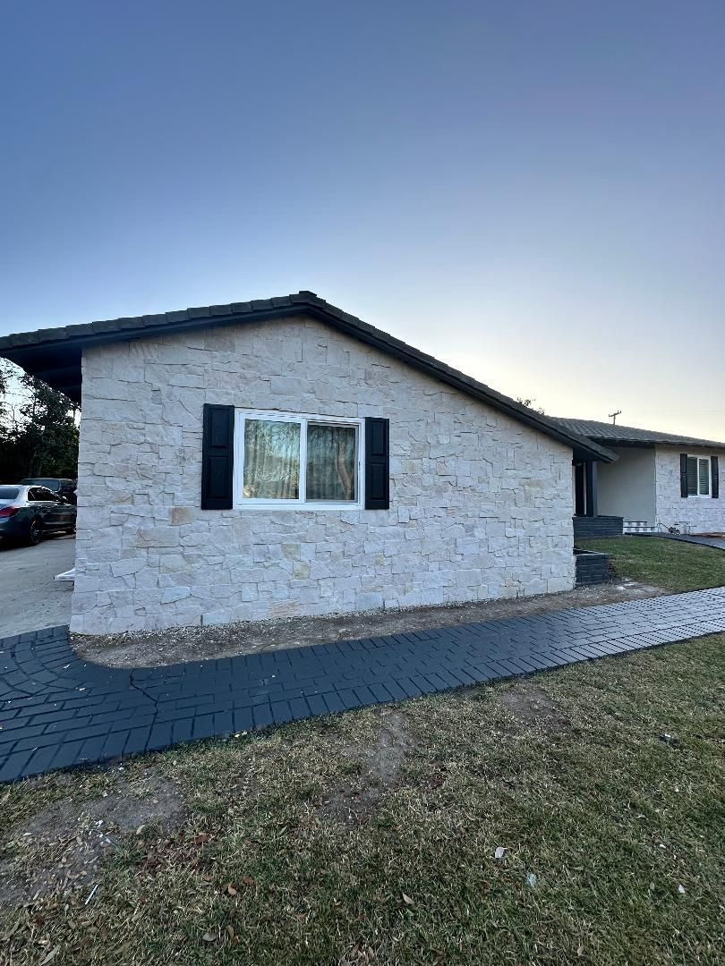 A white house with black shutters and a walkway in front of it.