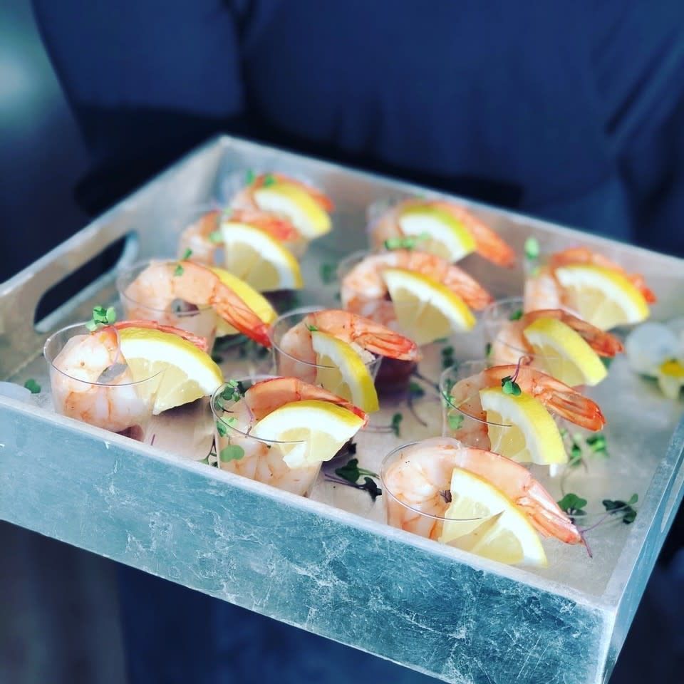 A person is holding a tray of shrimp cocktails with lemon slices.