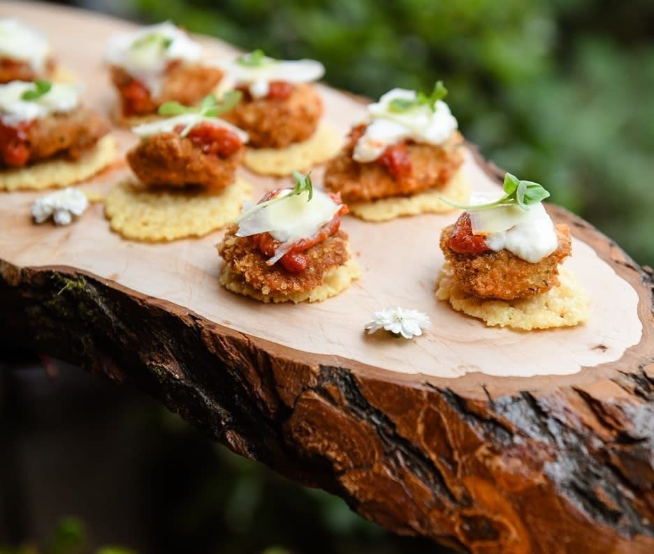 A wooden cutting board topped with appetizers on a piece of wood.