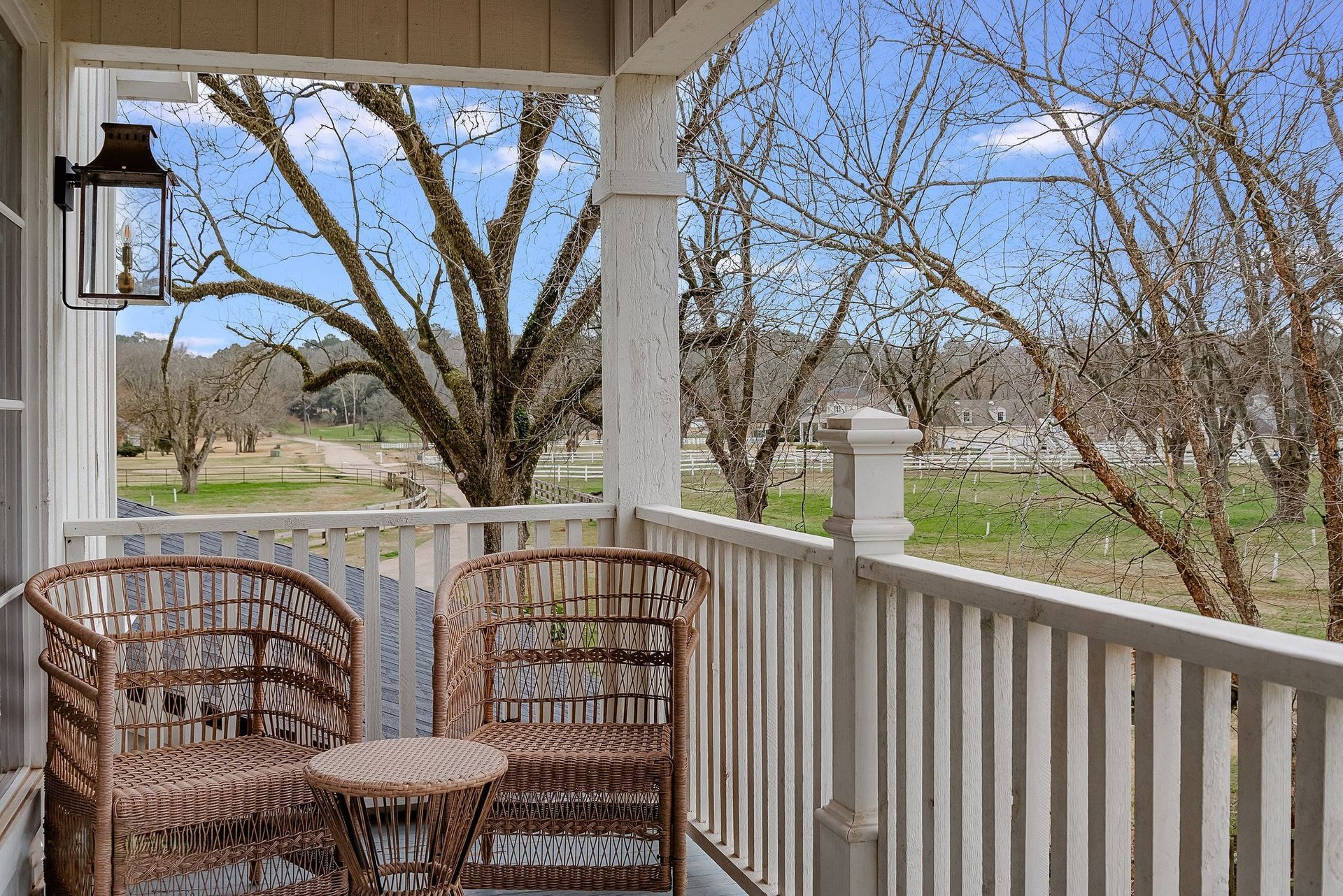 Porch with wicker chairs, white railing, and a view of trees and lawn